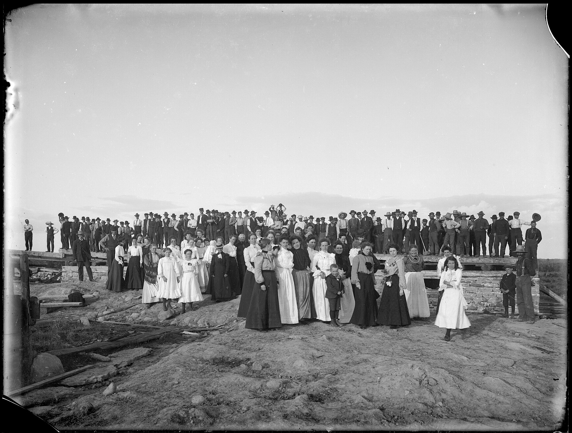 A crowd of people gathered to raise the timber frame of a barn